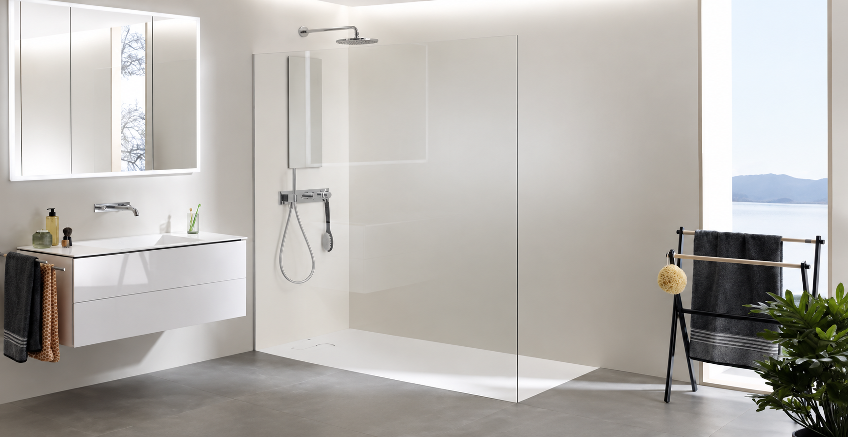 Modern bathroom featuring a frameless glass shower enclosure, floating white vanity, chrome fixtures, illuminated mirror, gray tile flooring, and minimalist decor with natural plants and dark towels.